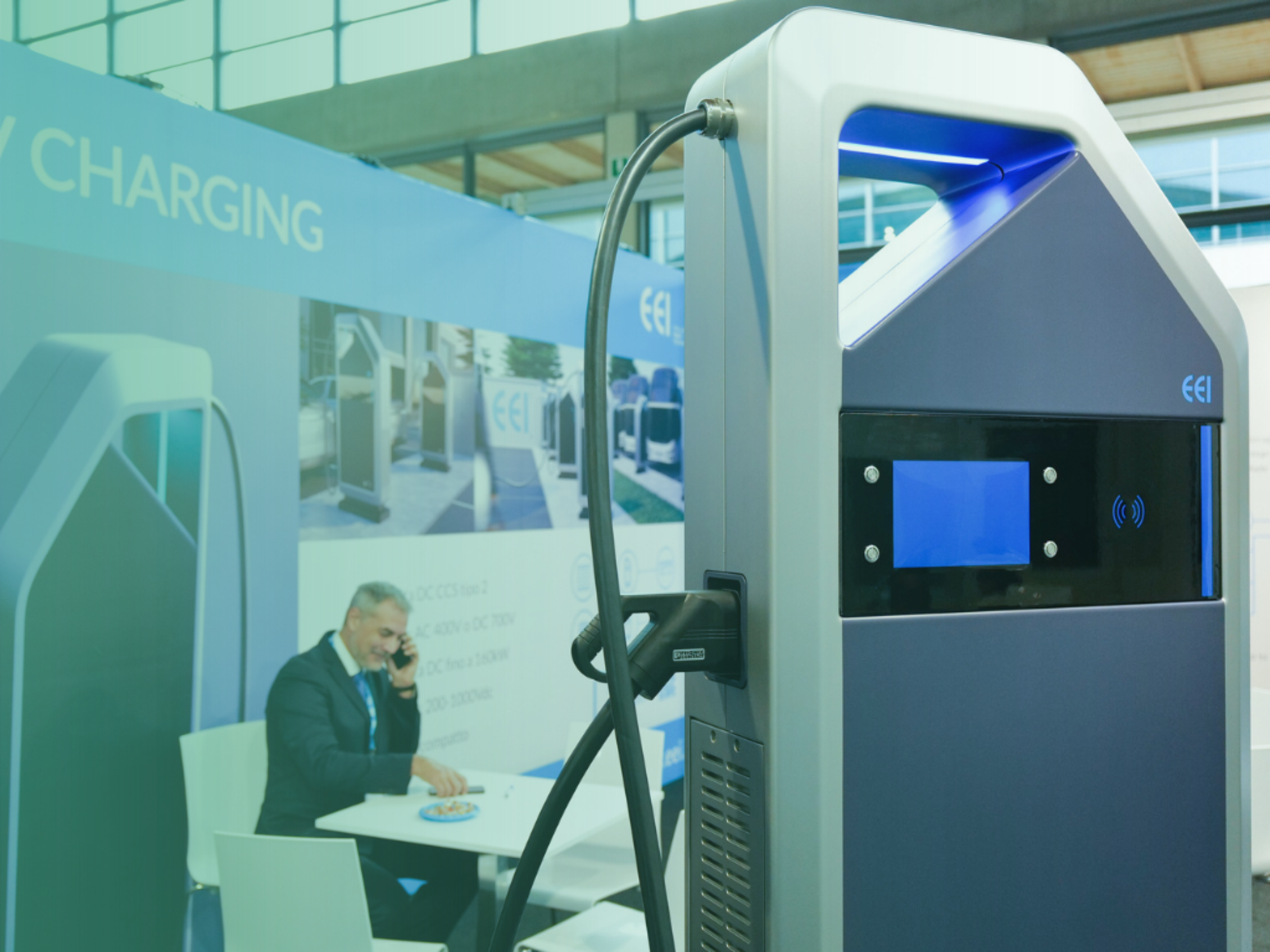 Colonnina di ricarica elettrica esposta con persona seduta allo stand.﻿